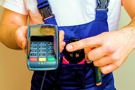 Contractors in Florida - Merchant Credit Card and ACH Processing, in photo a man in work overhauls and a t-shirt is holding a credit card swiper machine to get paid.