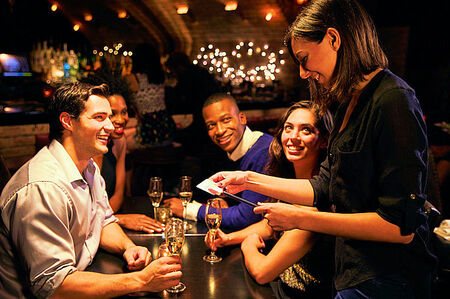 Restaurants in Florida - Merchant Credit Card and ACH Processing - Pictured is a waitress swiping a credit card on a tablet in front of two couples at dinner at a restaurant.