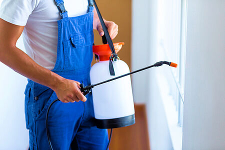 Merchant Credit Card and ACH Processing for Exterminators in Florida, in Photo Man in white t-shirt and blue overalls spaying buy spray indoors by a window.