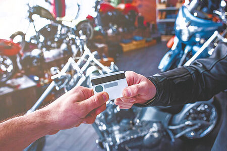Merchant Credit Card and ACH Processing for Motorcycle Shops in Florida, pictured is one man handing another man a credit card standing front of a motorcycle at a dealer.