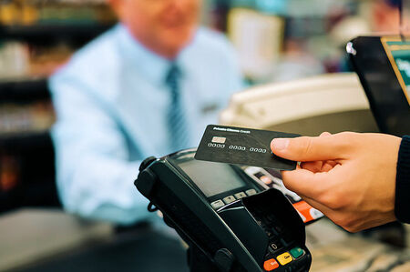 Retail Stores - Merchant Credit Card and ACH Processing - Credit Card Reader with person holding a credit card at the checkout counter of a retail store.